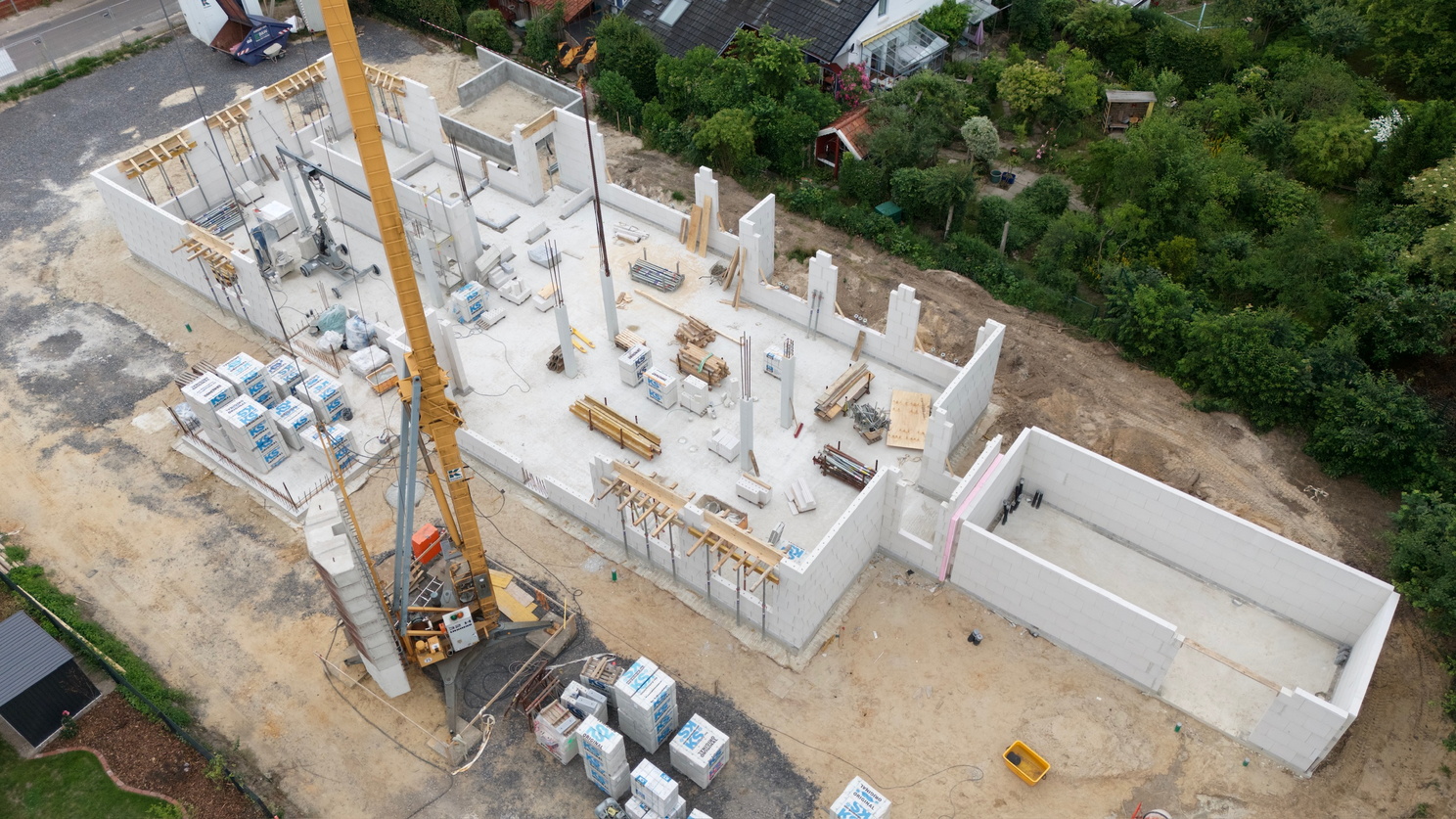 Eine Baustelle mit bereits hochgezogenen Mauern und einem Baukran ist aus der Vogelperspektive zu sehen.