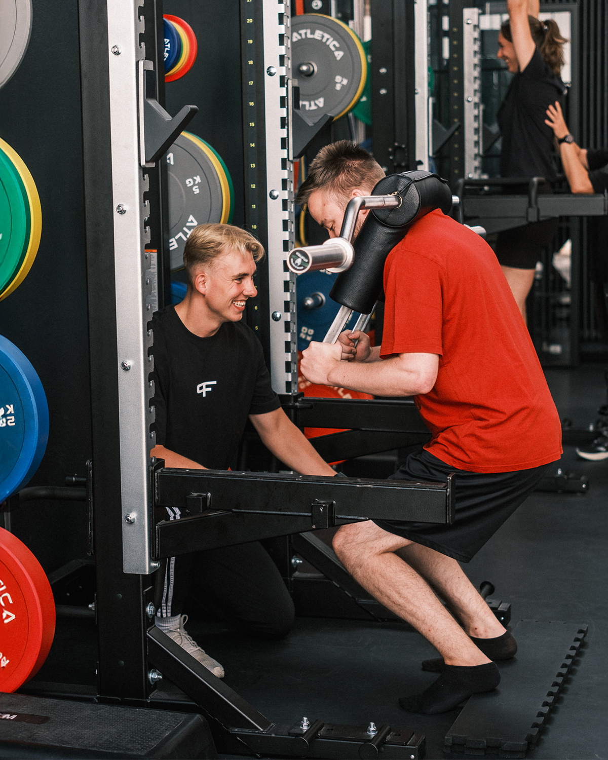 Ein Trainer unterstützt einen jungen Mann bei einer Übung mit einer Kettlebell im Ausfallschritt