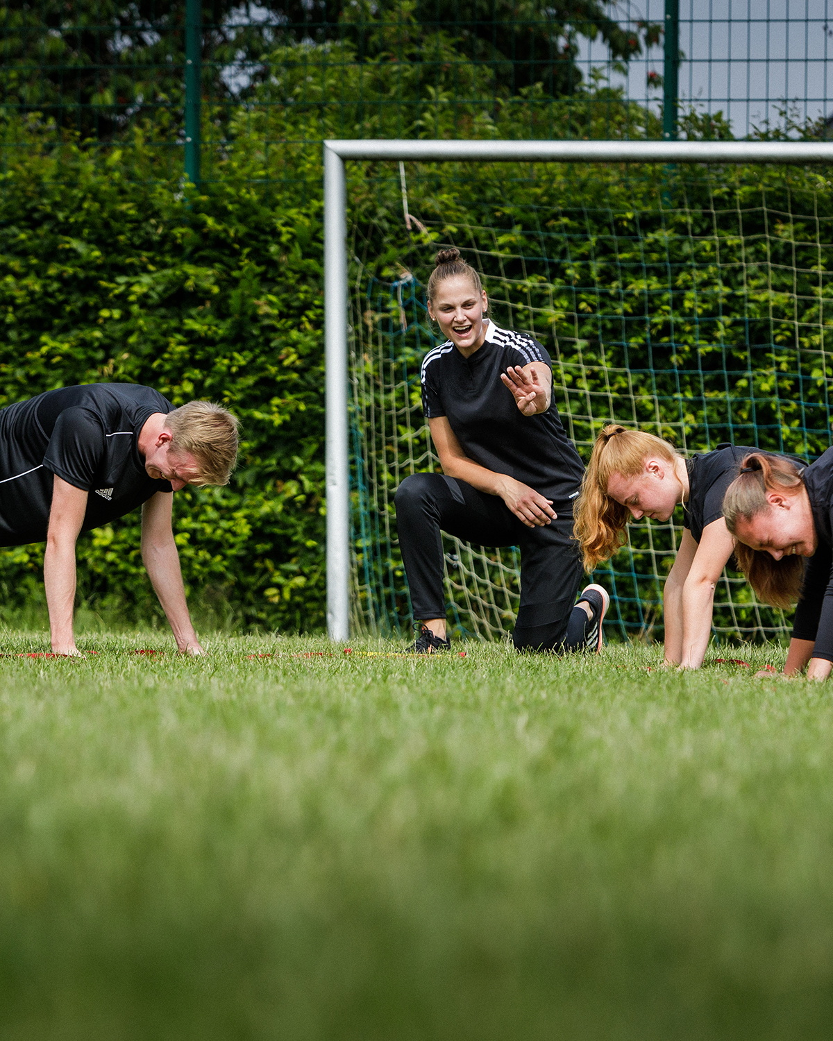 Eine Person trainiert auf einer Wiese mit einem Medizinball, während im Hintergrund weitere Personen Sport treiben