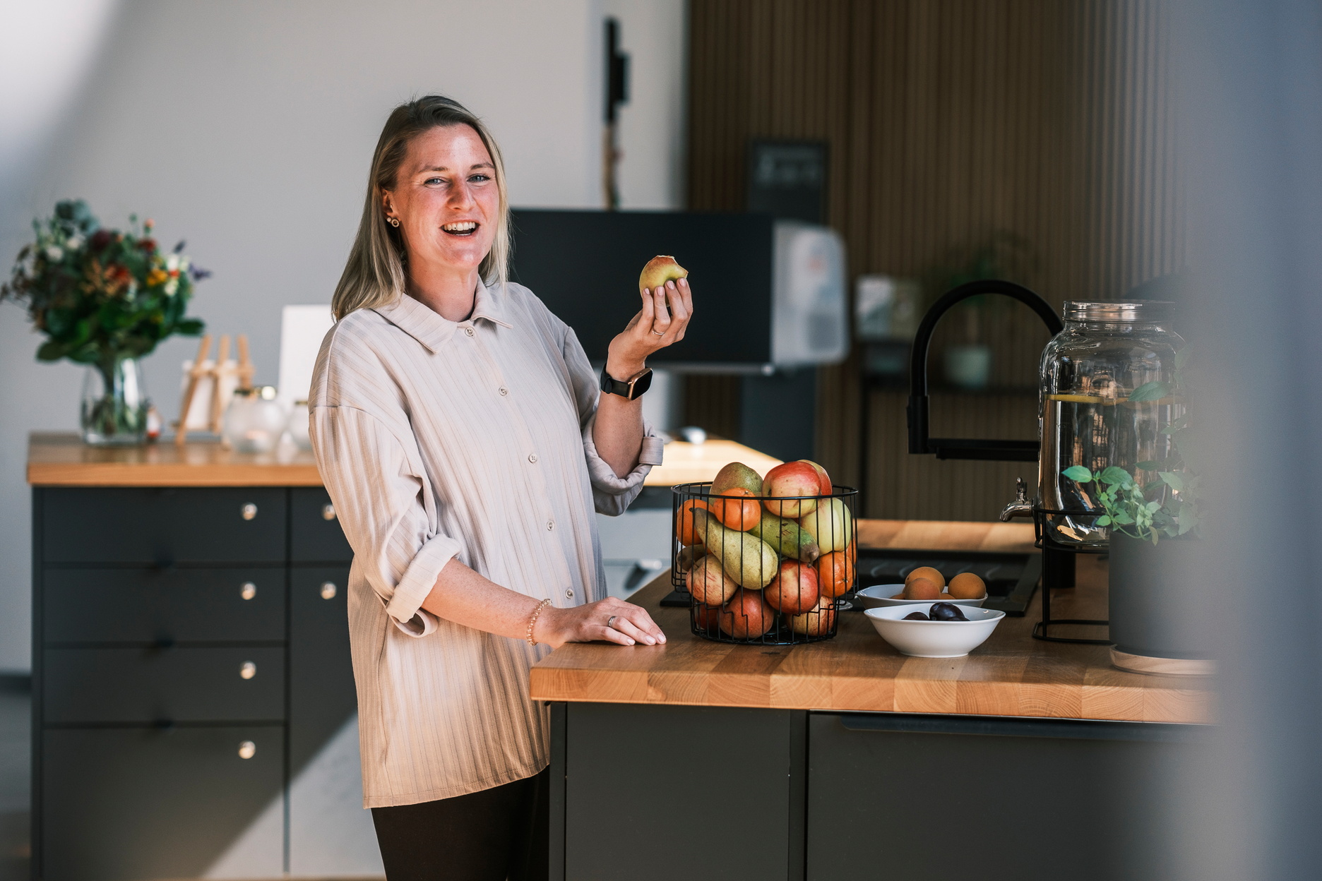 Eine Frau hält einen Apfel in der Hand und steht vor einem Obstkorb