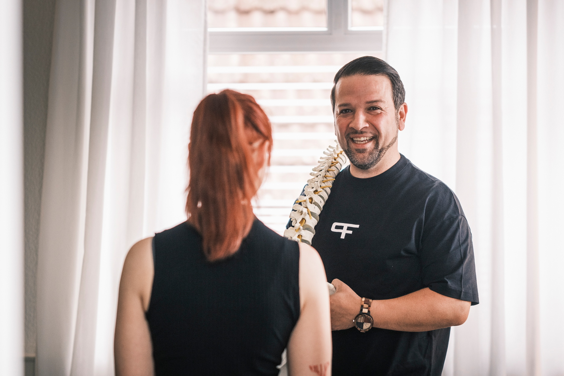 Ein Therapeut erklärt einer Patienten etwas an einem Wirbelsäulenmodell.