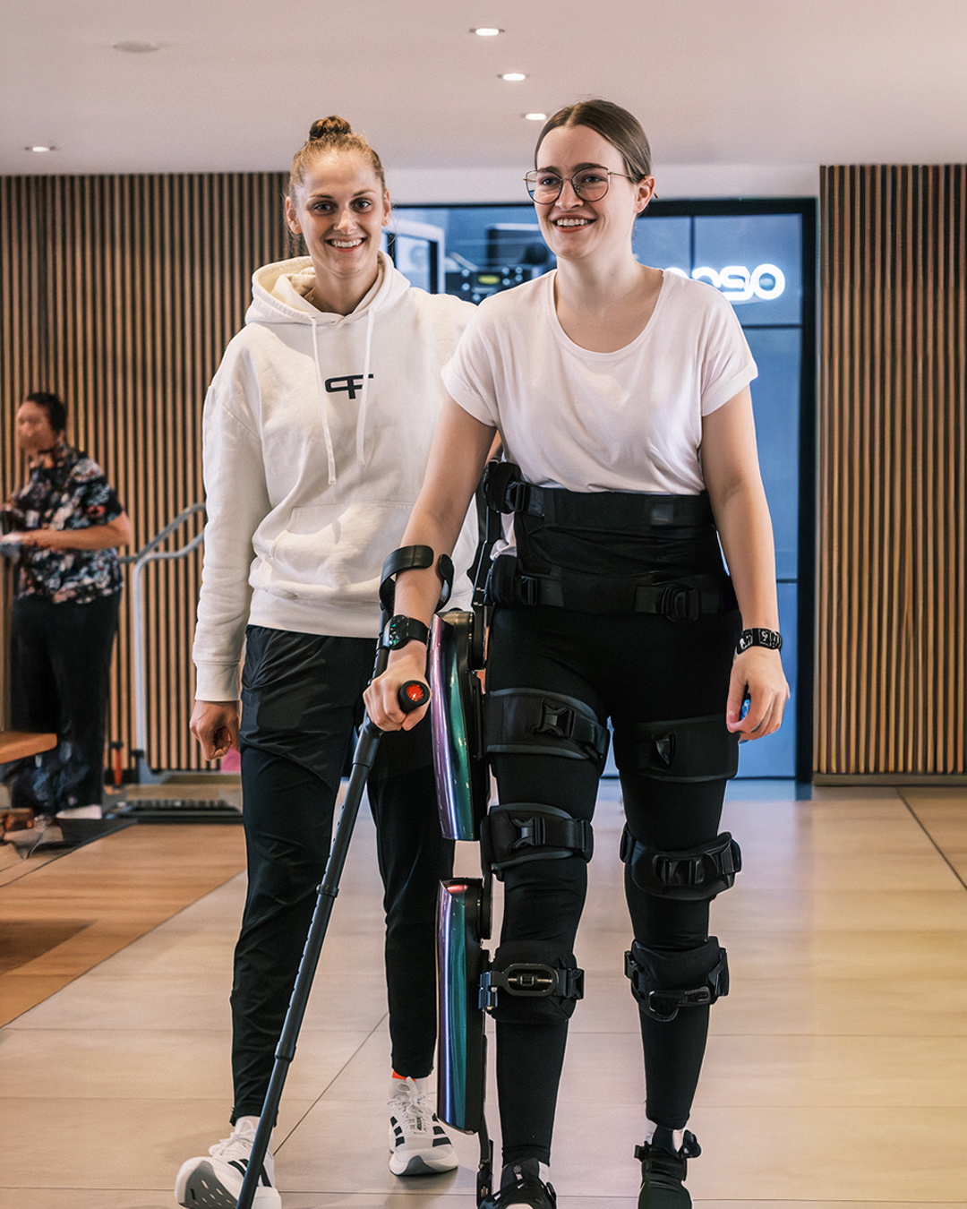 Eine Therapeutin begleitet eine Patientin beim Gehen mit einem Exoskelett