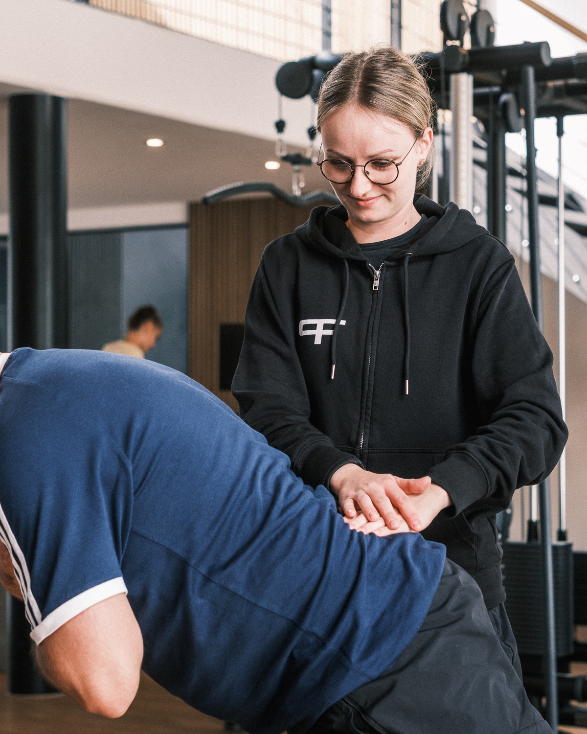 Eine Therapeutin behandelt den Rücken eines Patienten, der eine Übung durchführt.