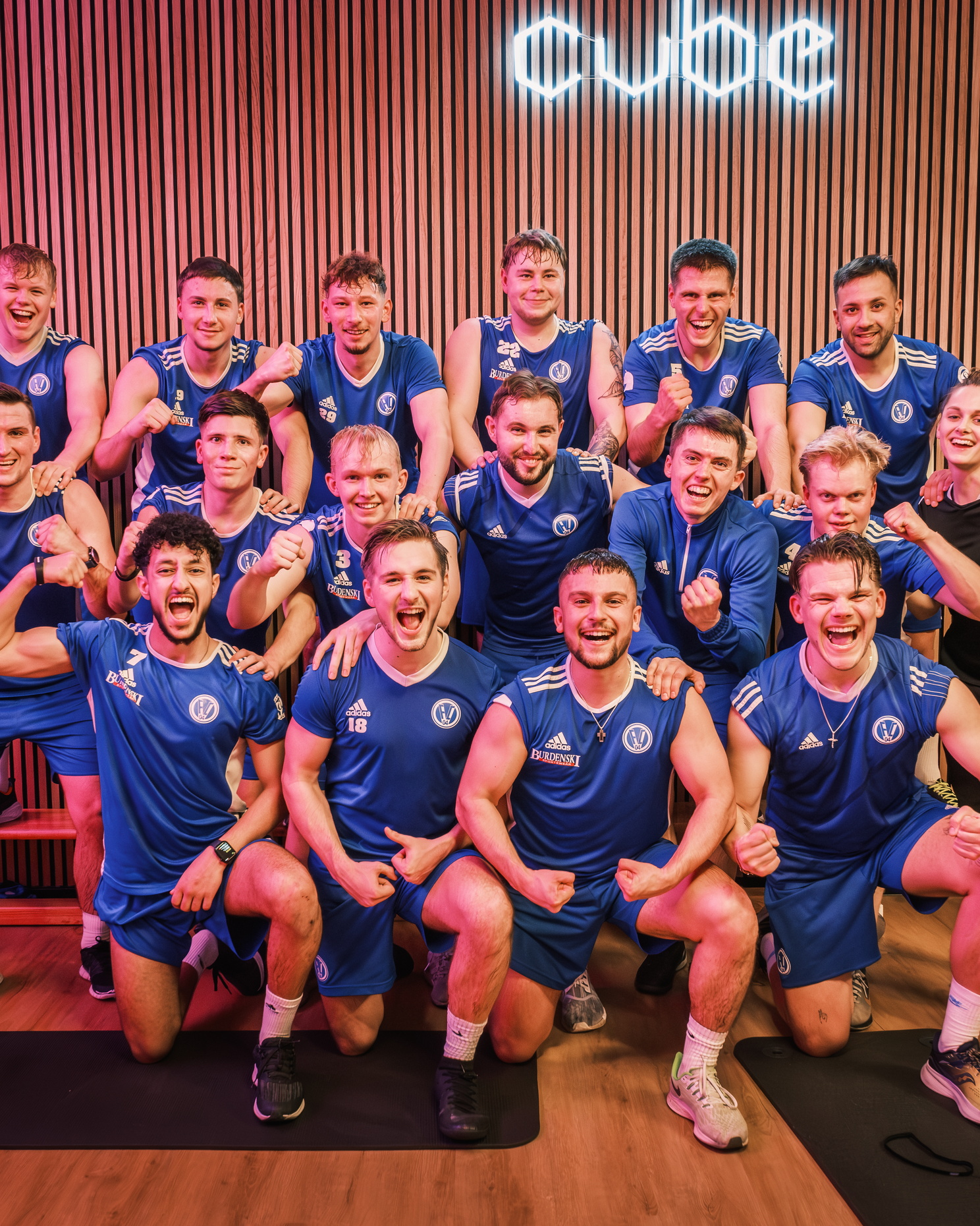 Eine Gruppe junger Sportler in blauer Trainingskleidung macht ein Mannschaftsfoto in einem modernen Trainingsraum