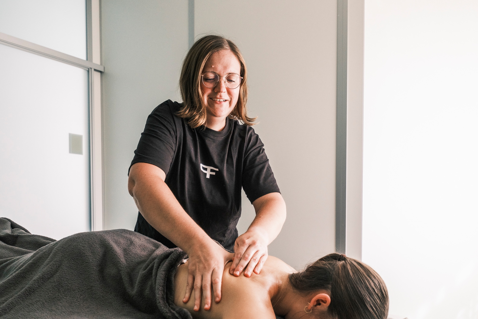 Eine Therapeutin massiert den Rücken einer liegenden Patientin.