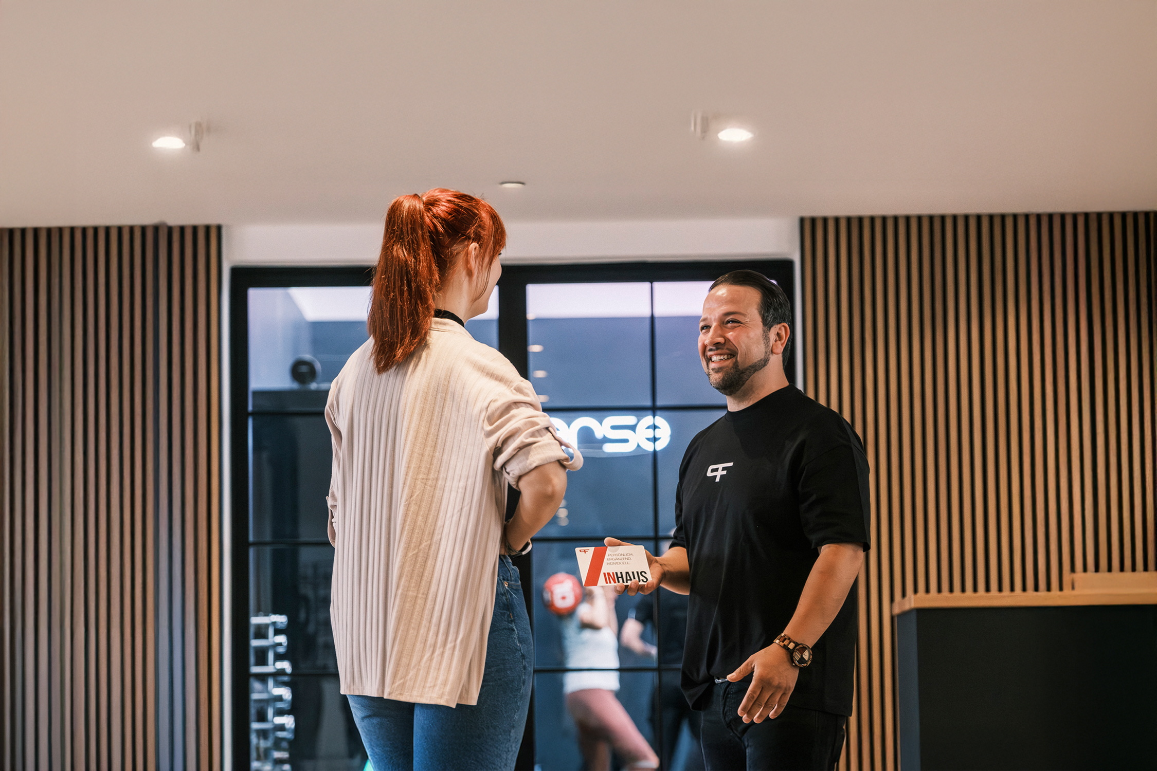 Zwei Personen stehen in einem modernen Trainingsraum und führen ein freundliches Gespräch.