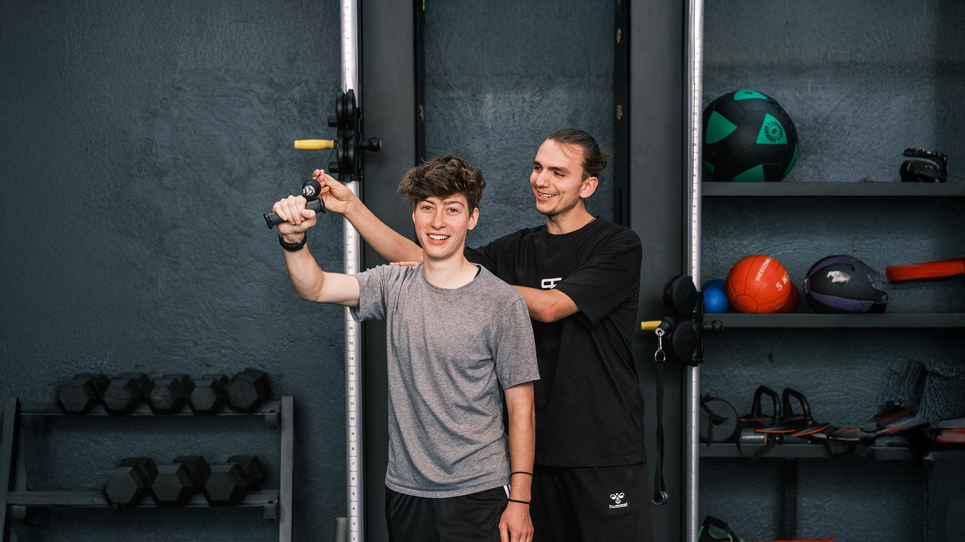Ein Trainer leitet eine Trainierende am Kabelzug an