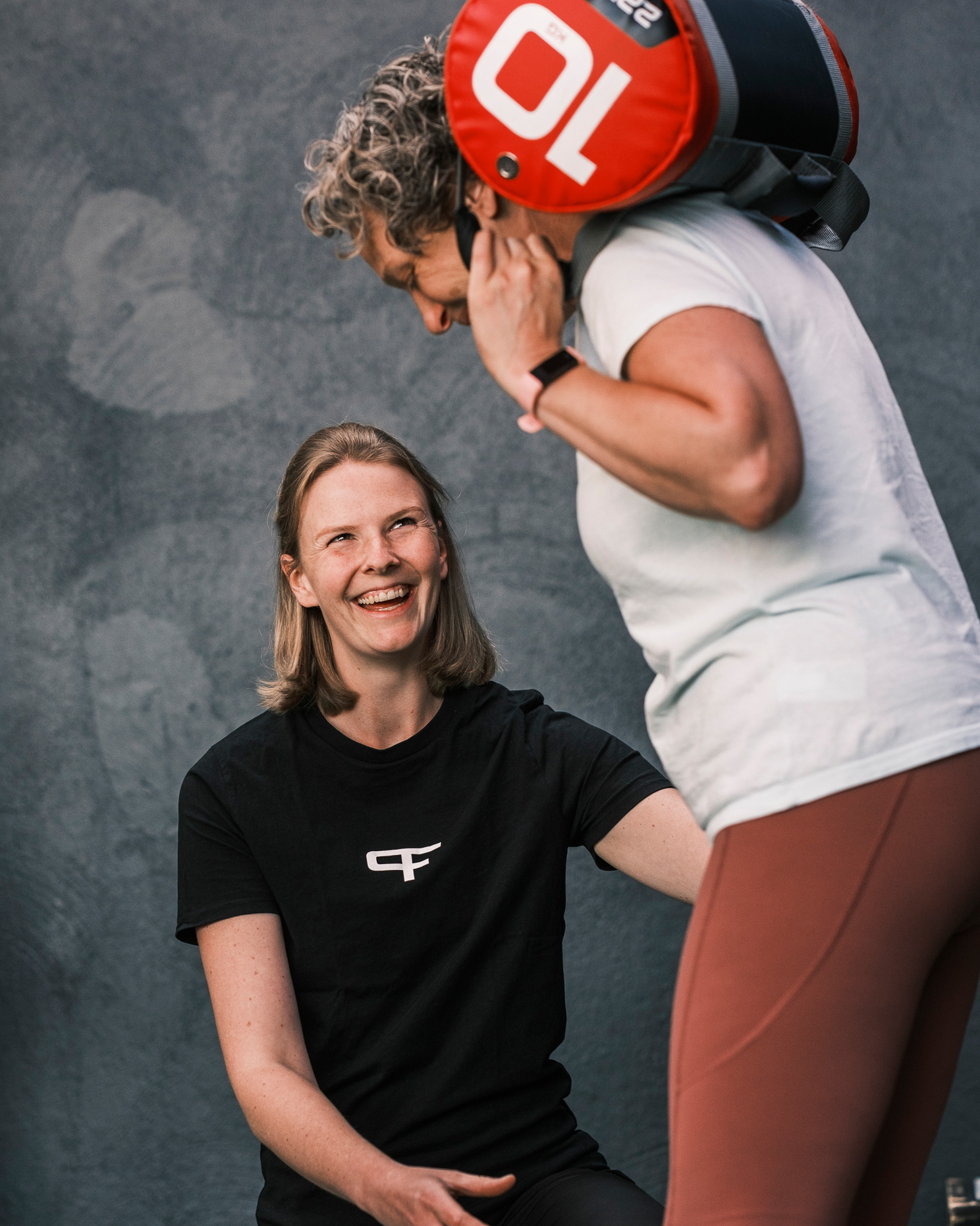 Eine Physiotherapeutin betreut eine Frau, die mit einem Trainingssack auf den Schultern eine Übung ausführt