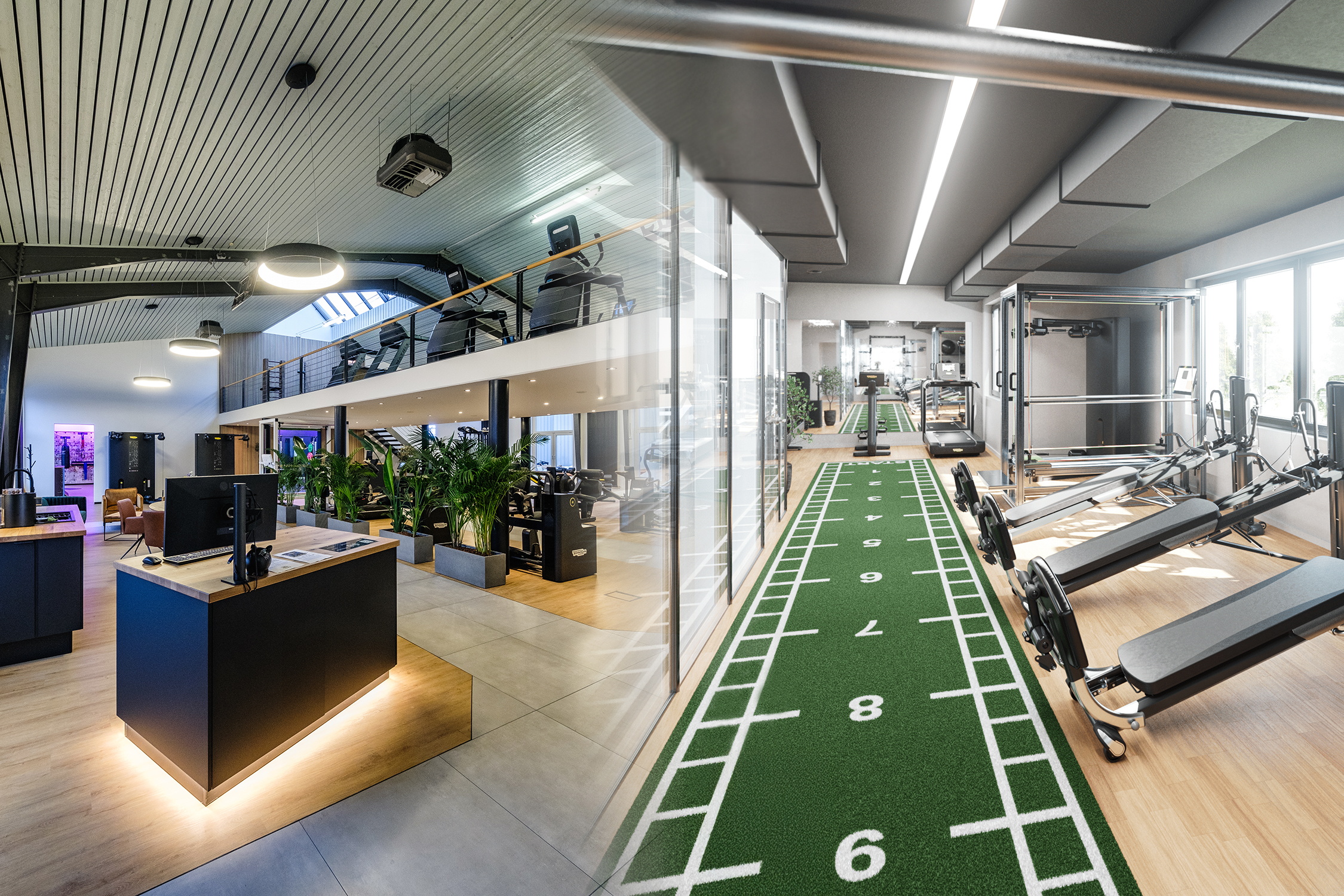 Ein modernes Trainingszentrum mit Empfangsbereich, Fitnessgeräten und einer grünen Sprintbahn