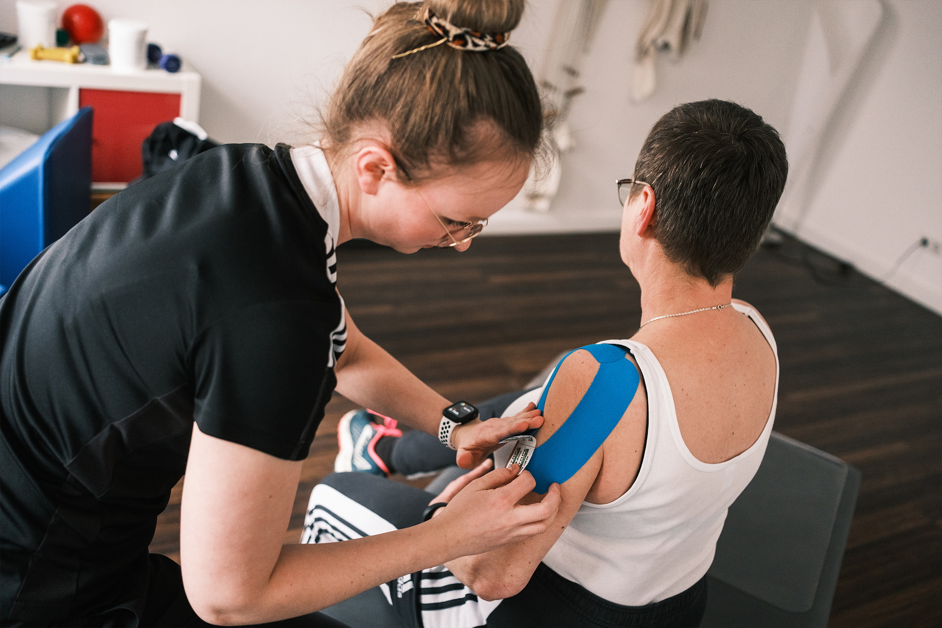 Eine Therapeutin bringt einen Tape auf der Schulter einer Patientin an.