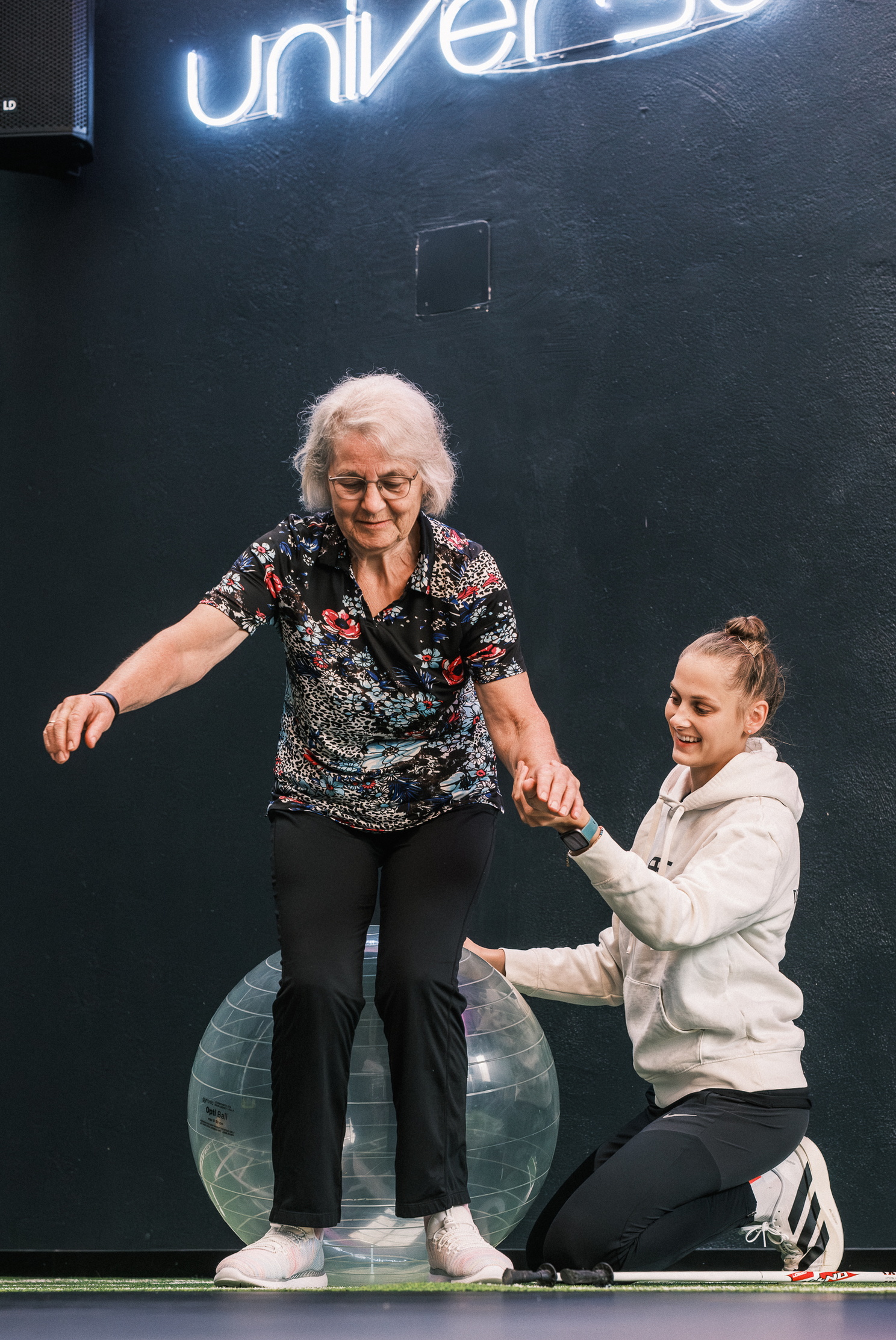 Eine Physiotherapeutin unterstützt eine ältere Frau beim Training mit einem Gymnastikball