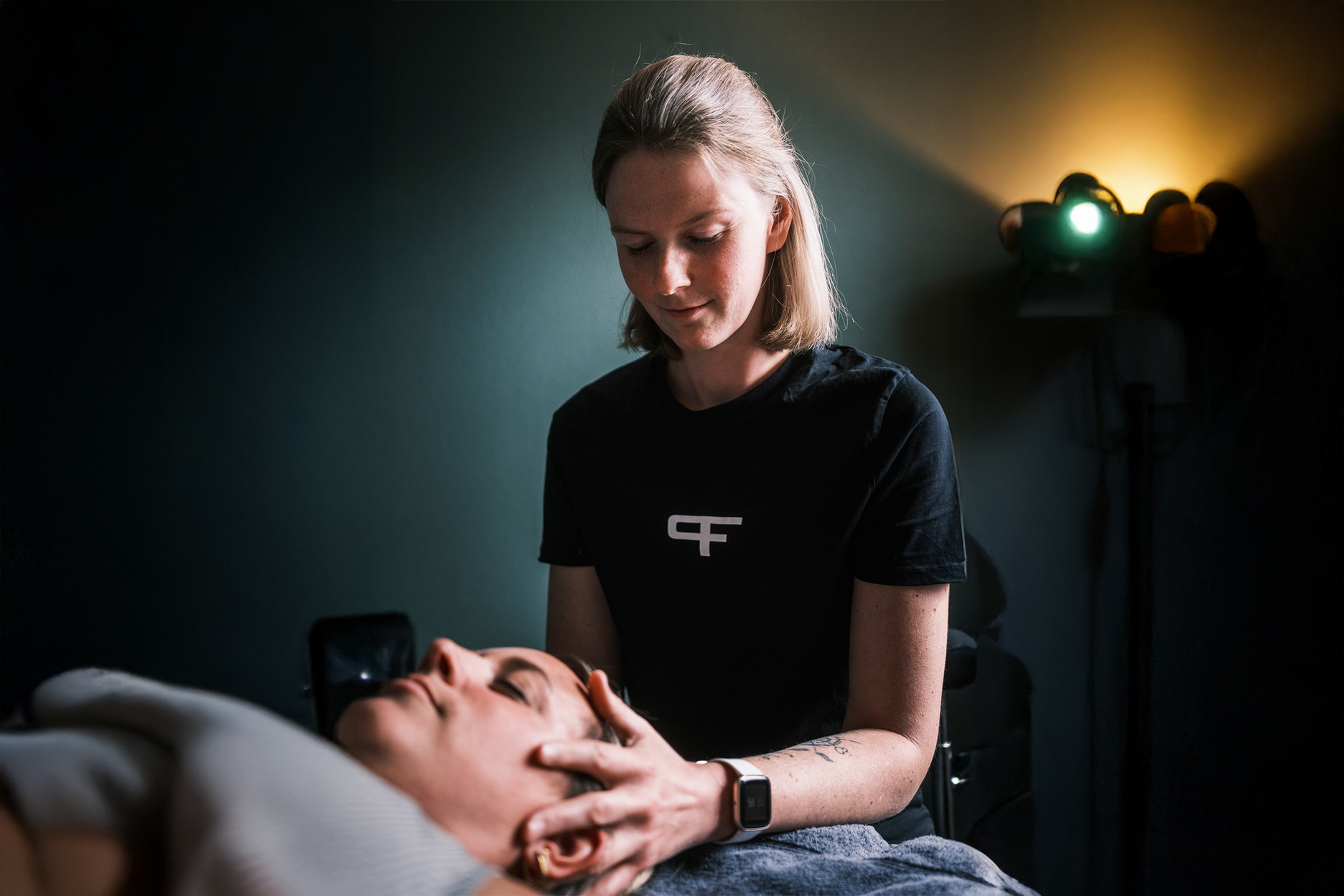 Eine Therapeutin behandelt den Kopf- und Kieferbereich einer liegenden Person.