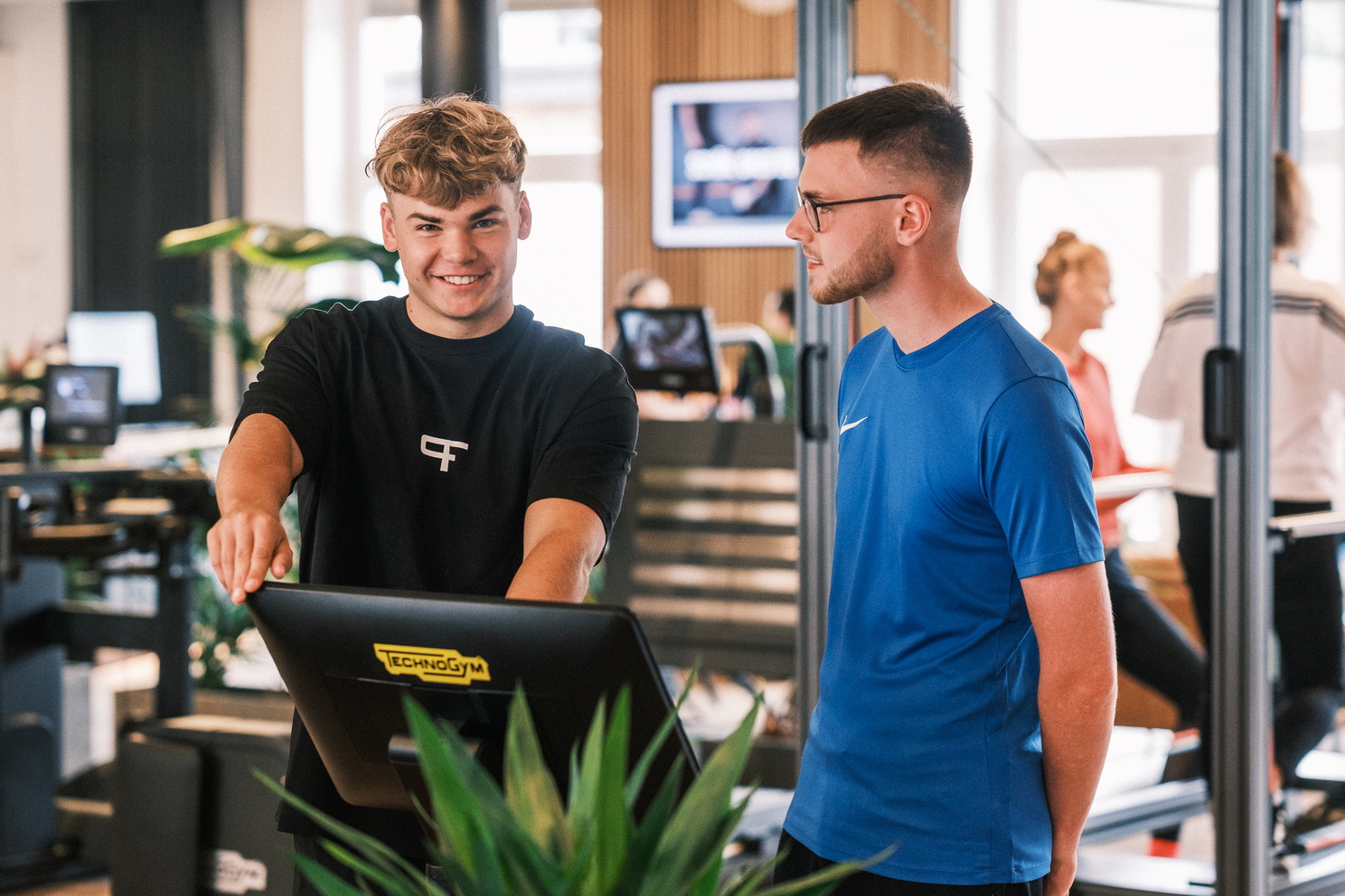 Ein Trainer erklärt einem Mann die Bedienung eines Fitnessgeräts mit Bildschirm