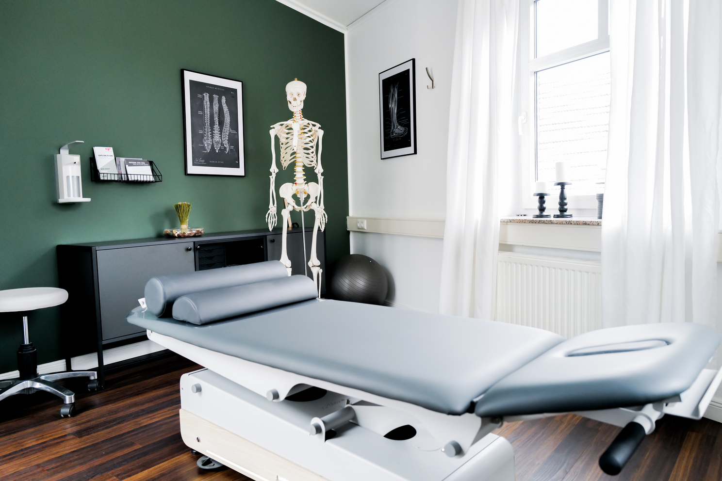 Ein Behandlungsraum mit einer Liege, einem Skelettmodell und anatomischen Wandpostern