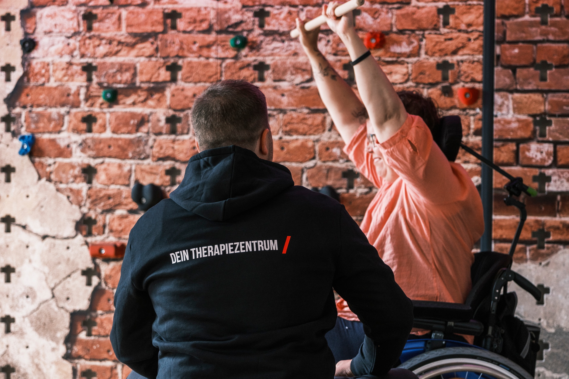 Eine Therapeut leitet eine Patienten im Rollstuhl zu einer Übung an.