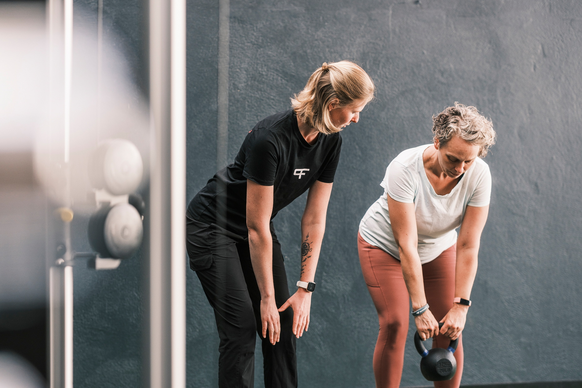 Eine Therapeutin begleitet eine Person bei einer Übung mit einer Kettlebell und achtet auf die richtige Bewegungsausführung.