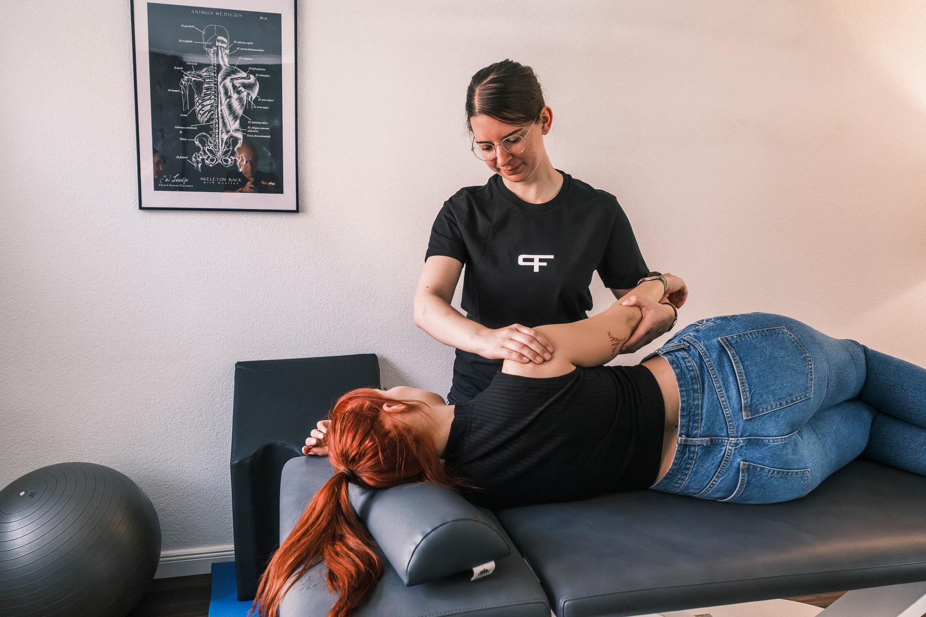 Eine Therapeutin behandelt eine Person auf einer Liege an der Schulter.
