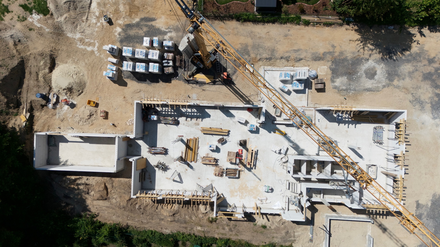 Eine Baustelle mit Fundament und ersten Mauern ist aus der Vogelperspektive zu sehen, ein Baukran ragt über die Fläche