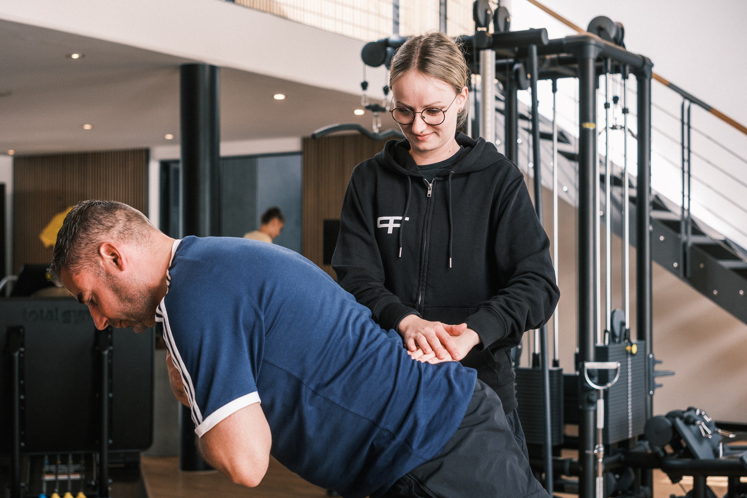 Eine Therapeutin unterstützt einen Patienten bei einer Übung, indem sie ihre Hände auf seinen Rücken legt