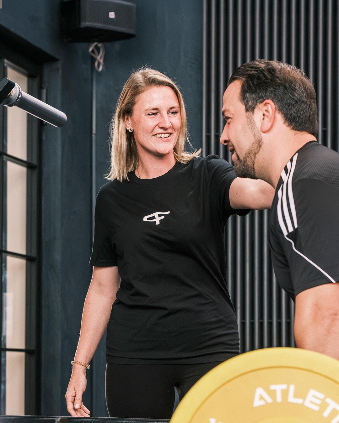 Eine Physiotherapeutin unterstützt einen Mann beim Training mit einer Langhantel