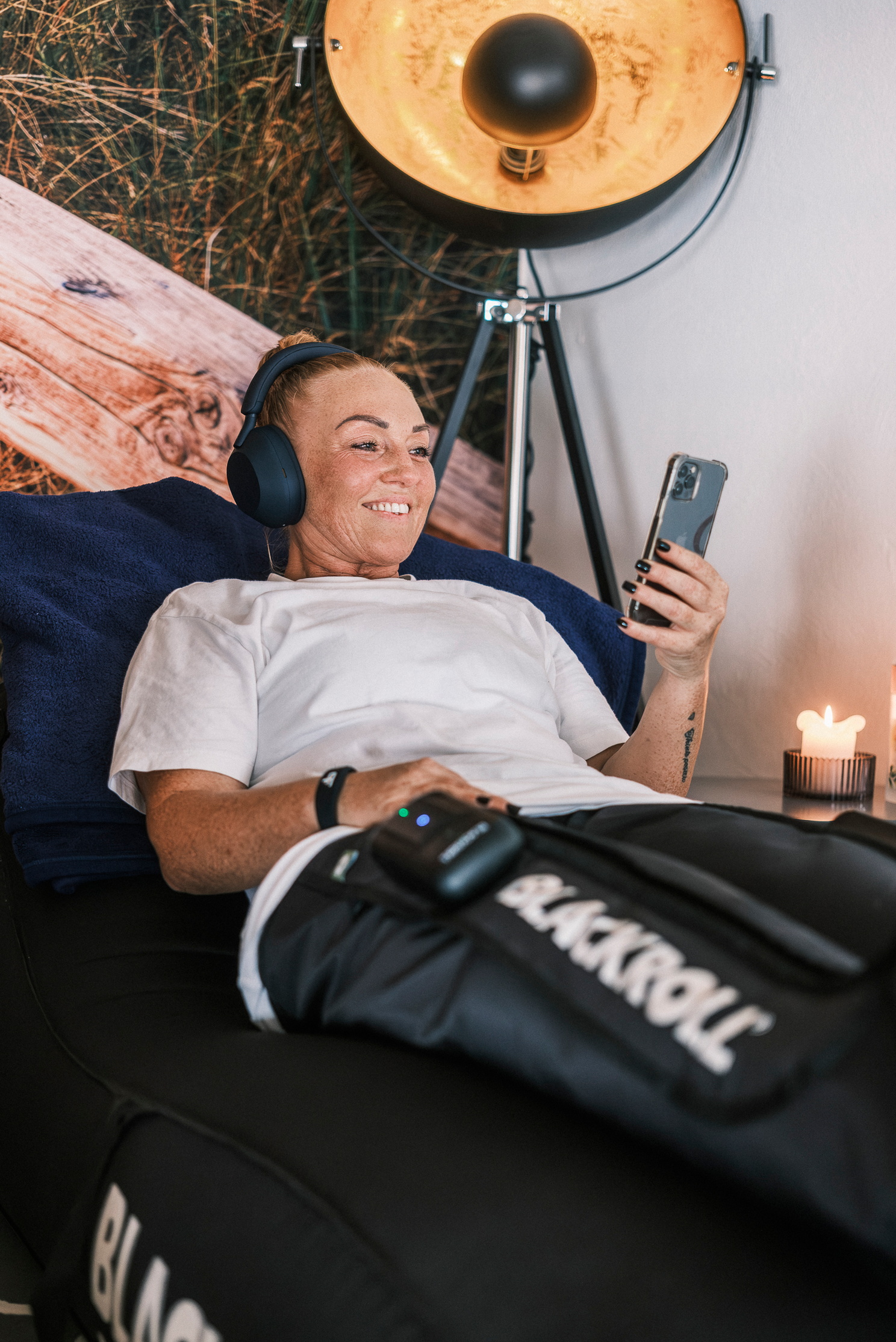 Eine Frau liegt entspannt mit Kopfhörern und schaut auf ihr Smartphone, während sie Kompressionsstiefel trägt