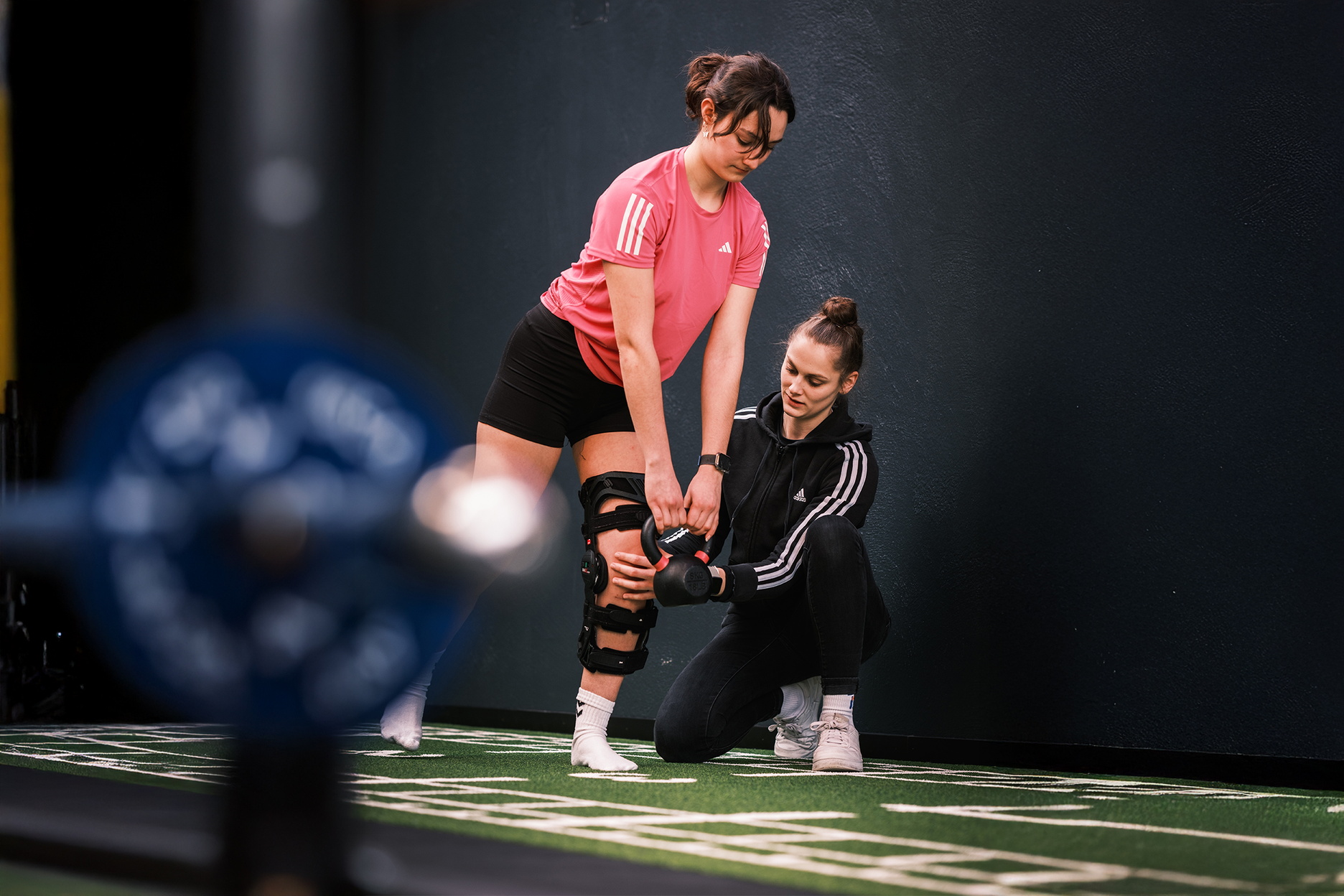 Eine Person mit Knieorthese führt unter fachlicher Anleitung eine Übung mit einer Kettlebell aus.