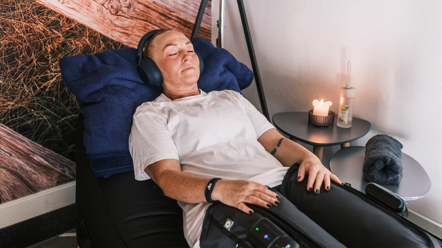 Eine Person mit geschlossenen Augen liegt auf einem Sessel und trägt Kopfhörer und Kompressionsstiefel
