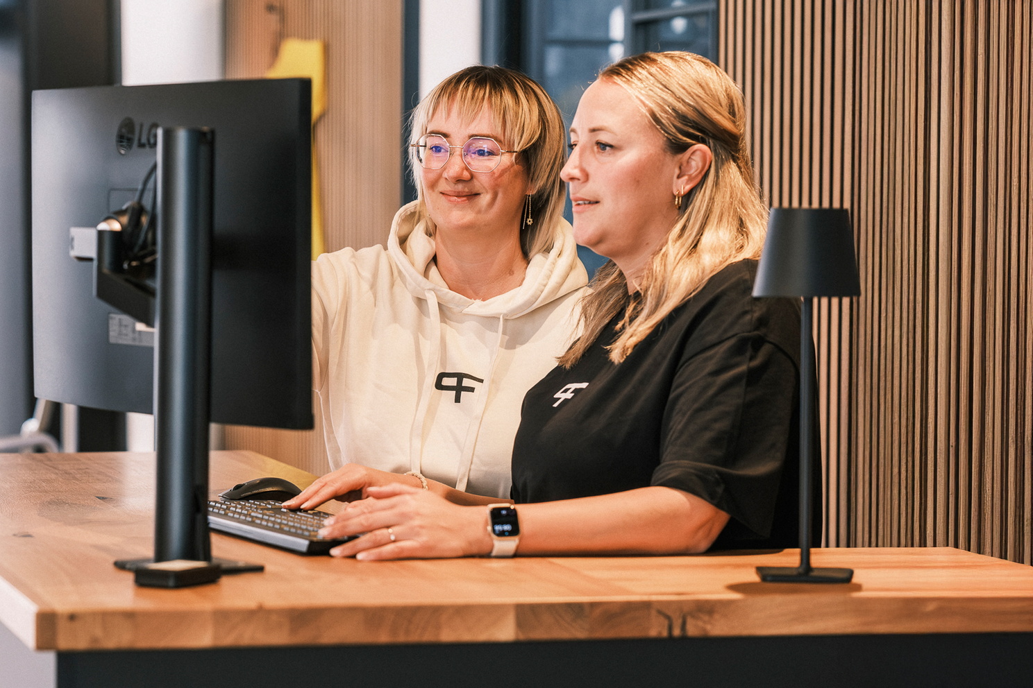 Zwei Mitarbeiterinnen arbeiten gemeinsam an einem Computerbildschirm am Empfang