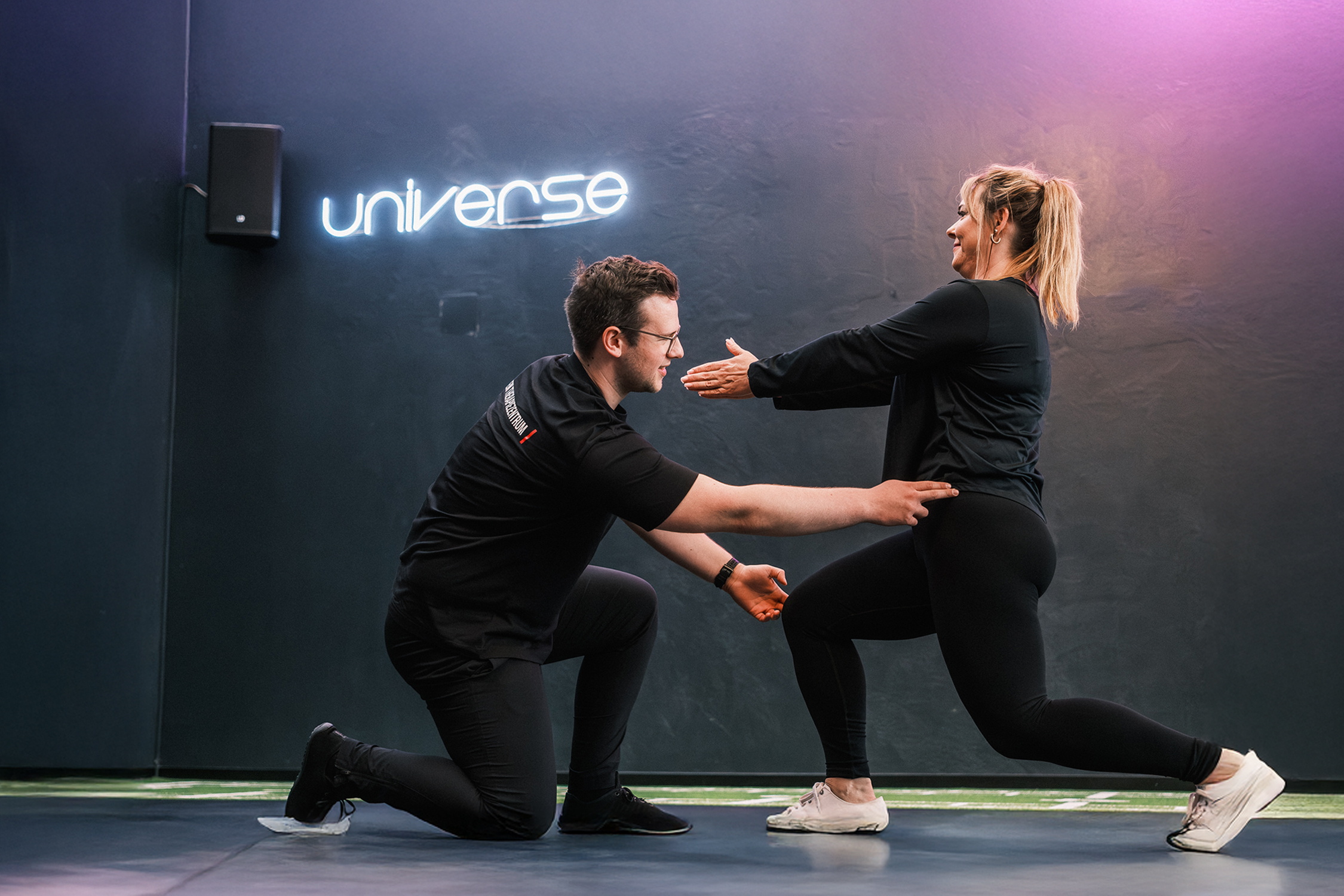 Ein Trainer unterstützt eine Frau bei einem Ausfallschritt im Trainingsraum