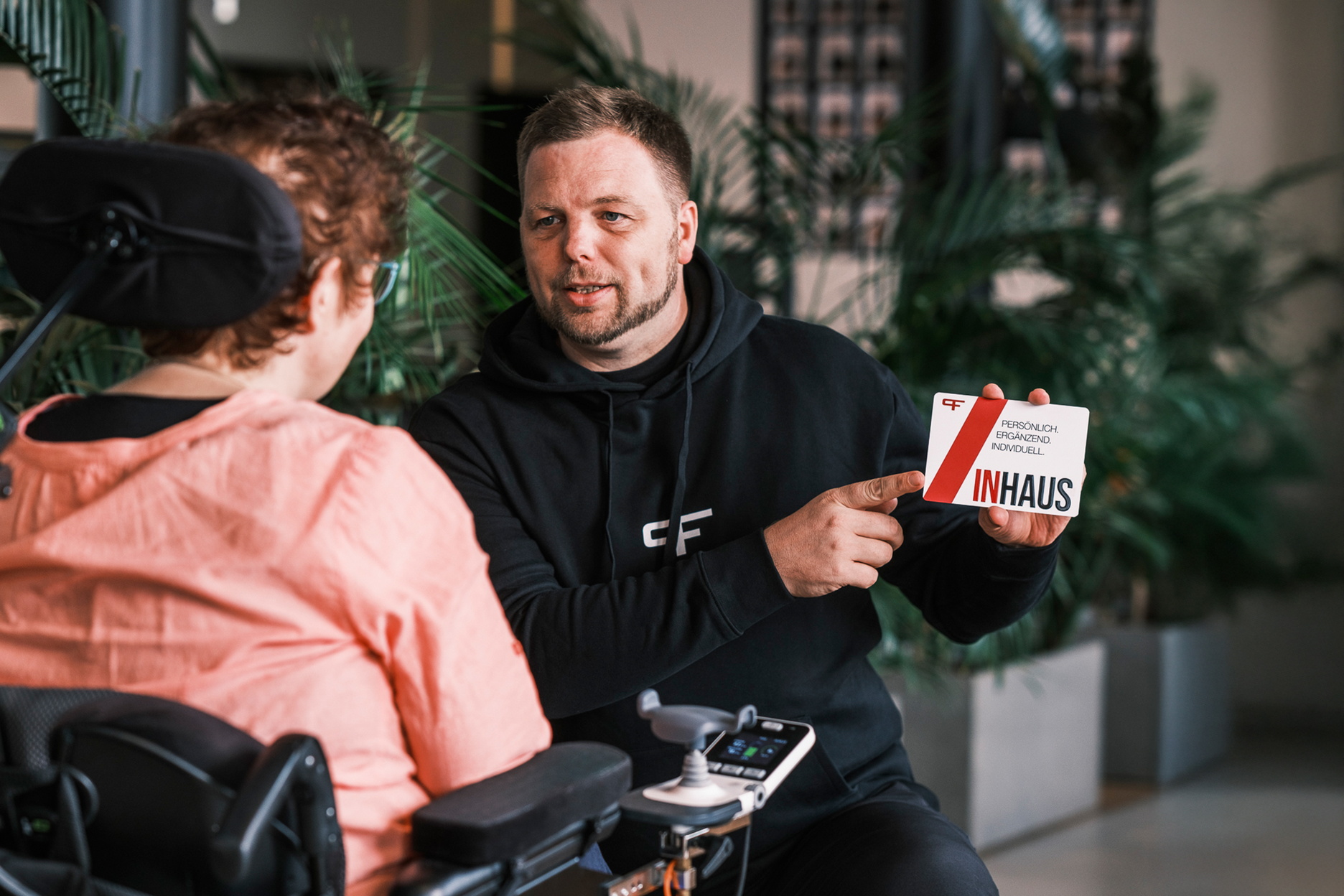 Ein Physiotherapeut erklärt einer Frau im Rollstuhl eine Informationskarte über ein Trainingskonzept