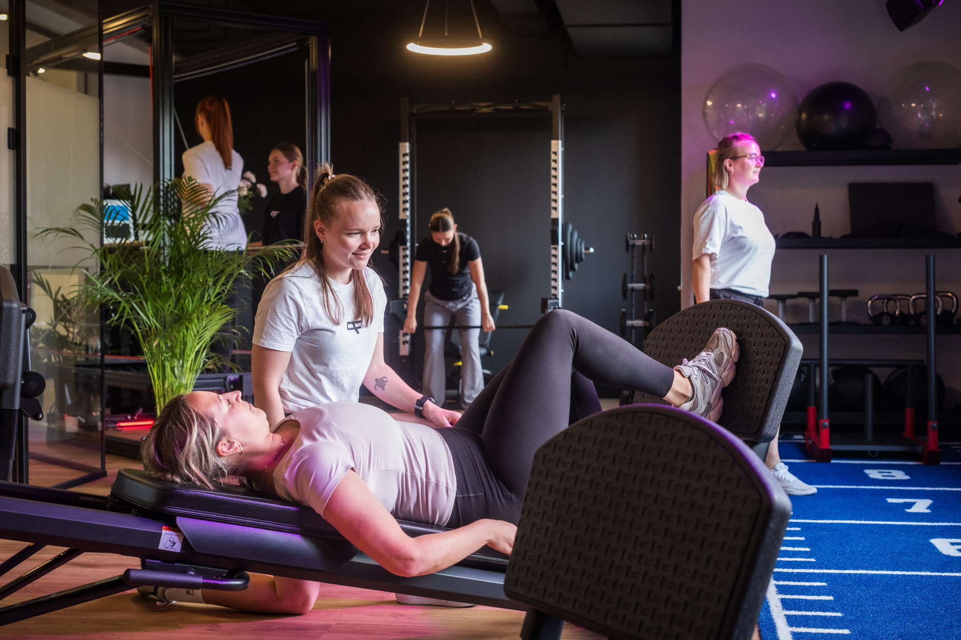 Mehrere Personen trainieren an Fitnessgeräten unter Anleitung einer Therapeutin.