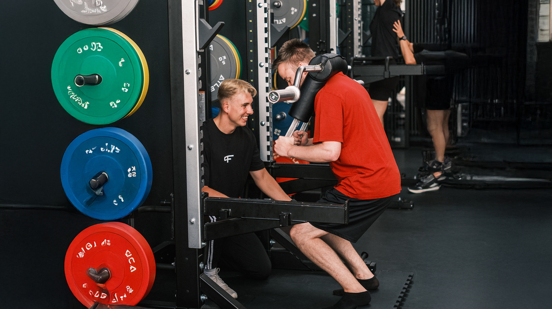 Ein Trainer unterstützt einen Mann beim Training an einem Gerät im Kraftraum