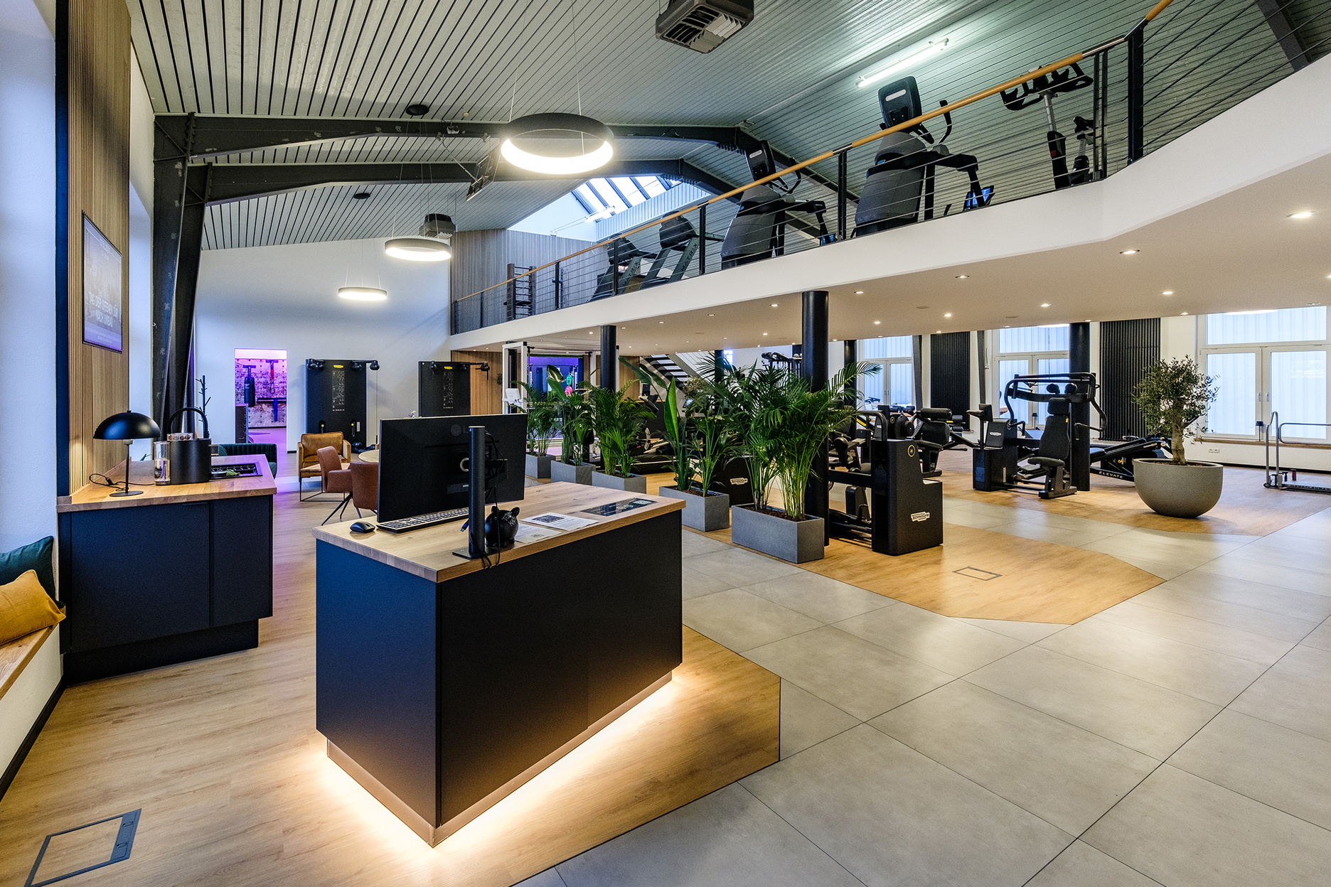 Ein moderner Trainingsraum mit Empfangstresen, Fitnessgeräten und einem zweiten Geschoss mit weiteren Trainingsgeräten